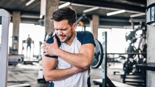 Opóżniona bolesność mięśni - mężczyzna na siłowni trzymający się za bolącą rękę.