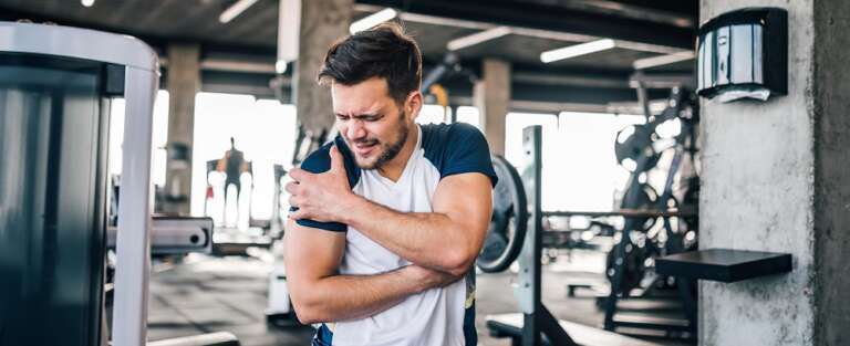 Opóżniona bolesność mięśni - mężczyzna na siłowni trzymający się za bolącą rękę.
